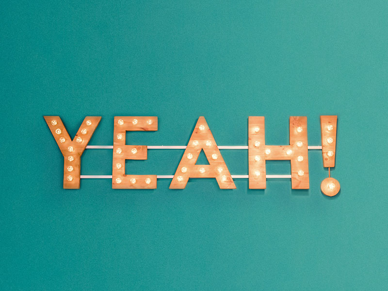 Illuminated marquee letters spelling "YEAH!" on a teal background.