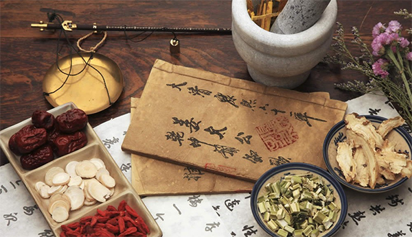 Traditional Chinese medicine herbs and ancient manuscripts on a wooden table.