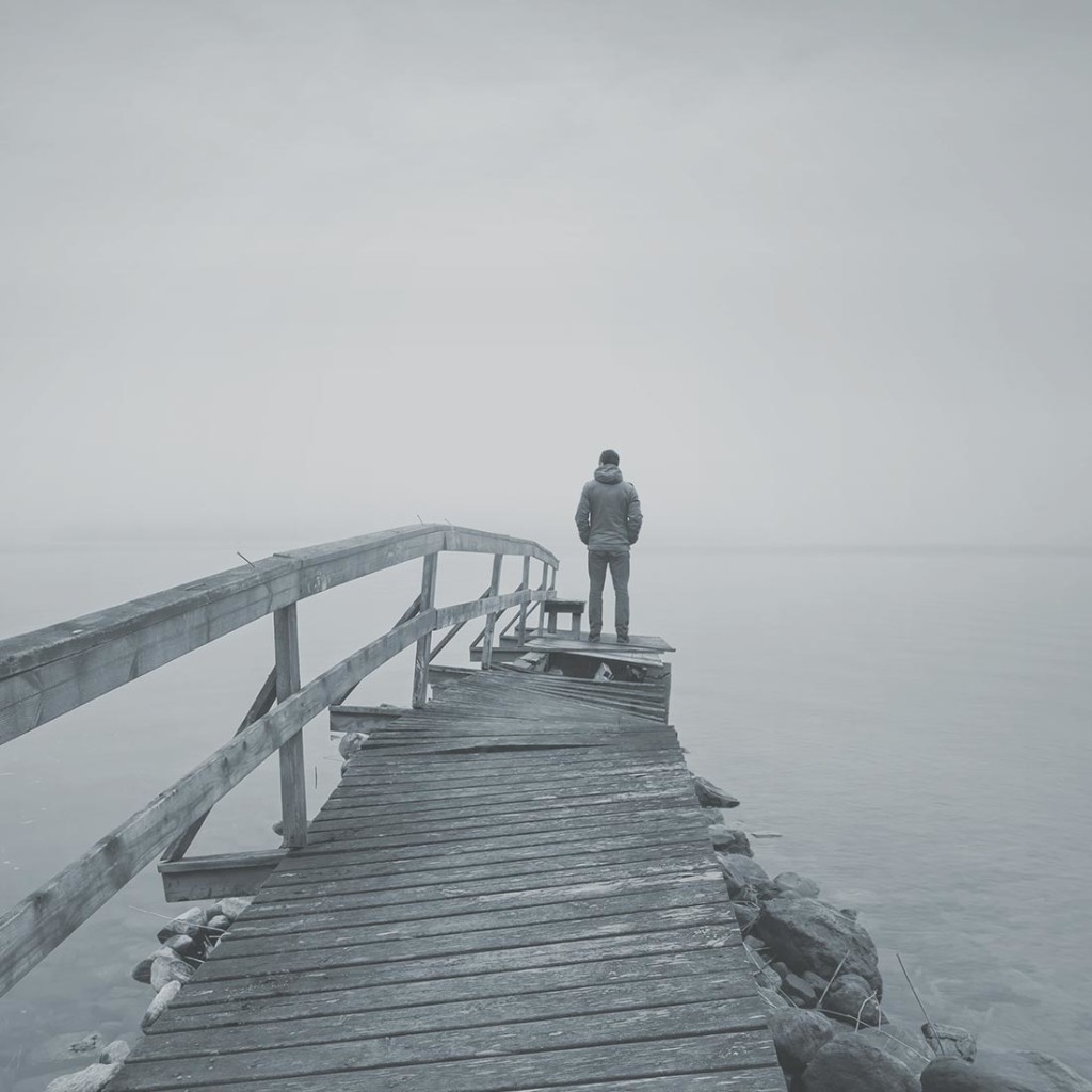 A solitary person standing at the end of a foggy wooden pier.