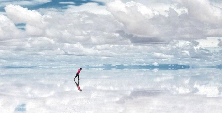 A person walking on a reflective water surface under a cloudy sky.
