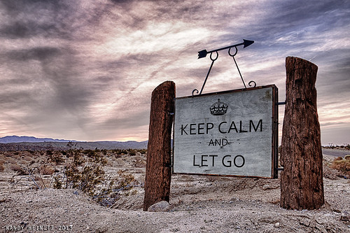 A rustic wooden sign reads 'Keep Calm and Let Go' in a desert landscape.