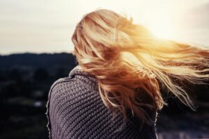 A woman with long blonde hair blowing in the wind at sunset.