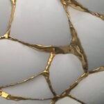 Close-up of white ceramic pieces joined by gold lacquer in a kintsugi style.