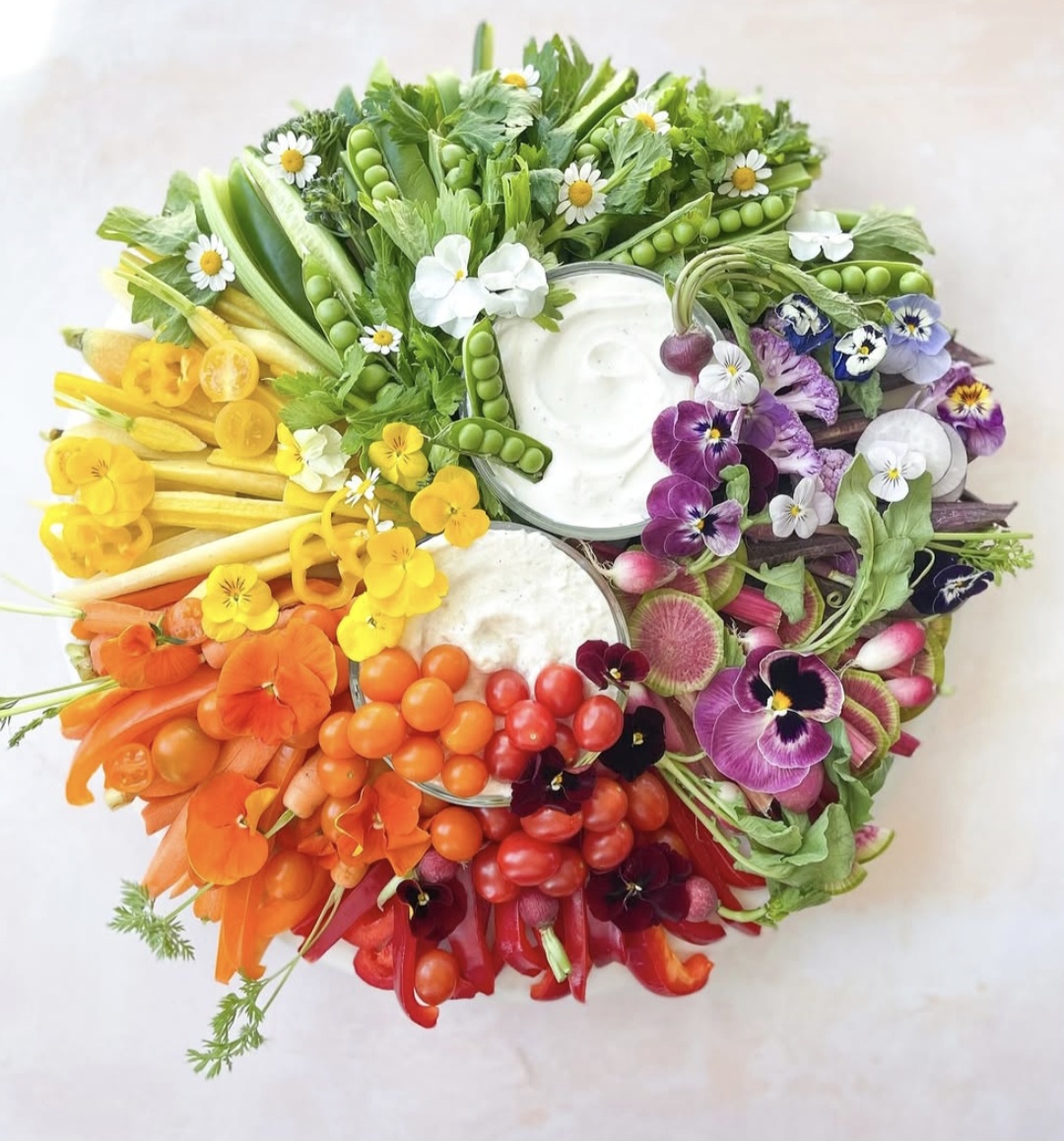 A colorful, circular arrangement of fresh vegetables and edible flowers.