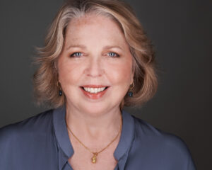 Smiling middle-aged woman with light hair and blue blouse.