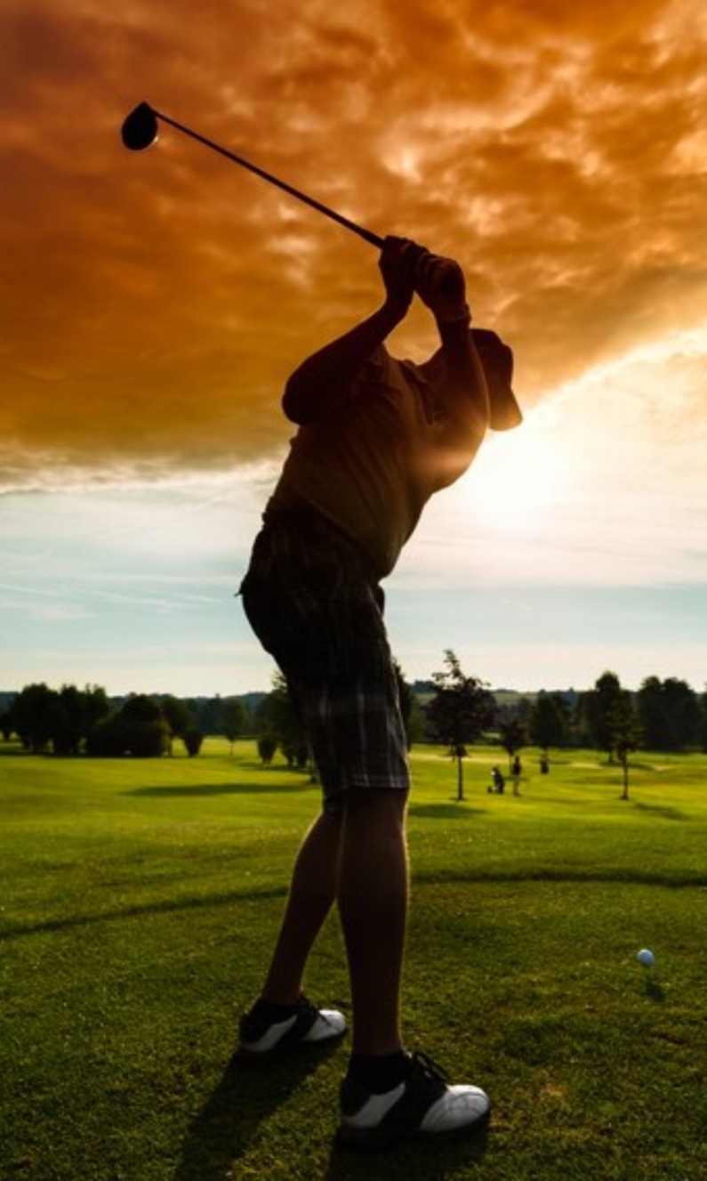 Golfer swinging club at sunset on a golf course.
