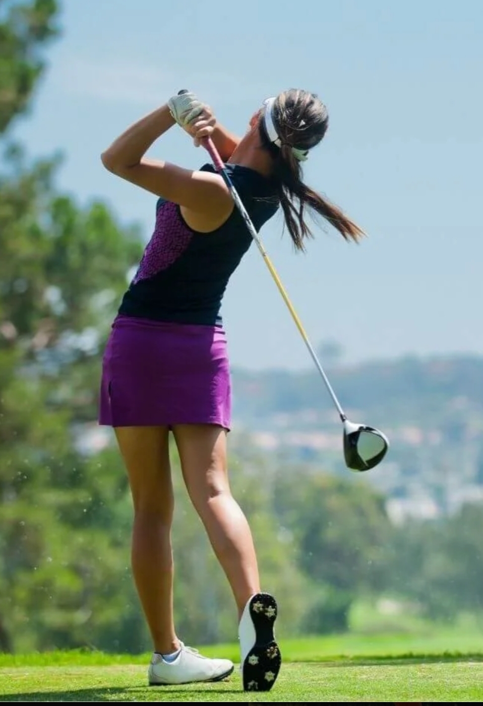 Woman in purple dress swinging a golf club on a sunny day.
