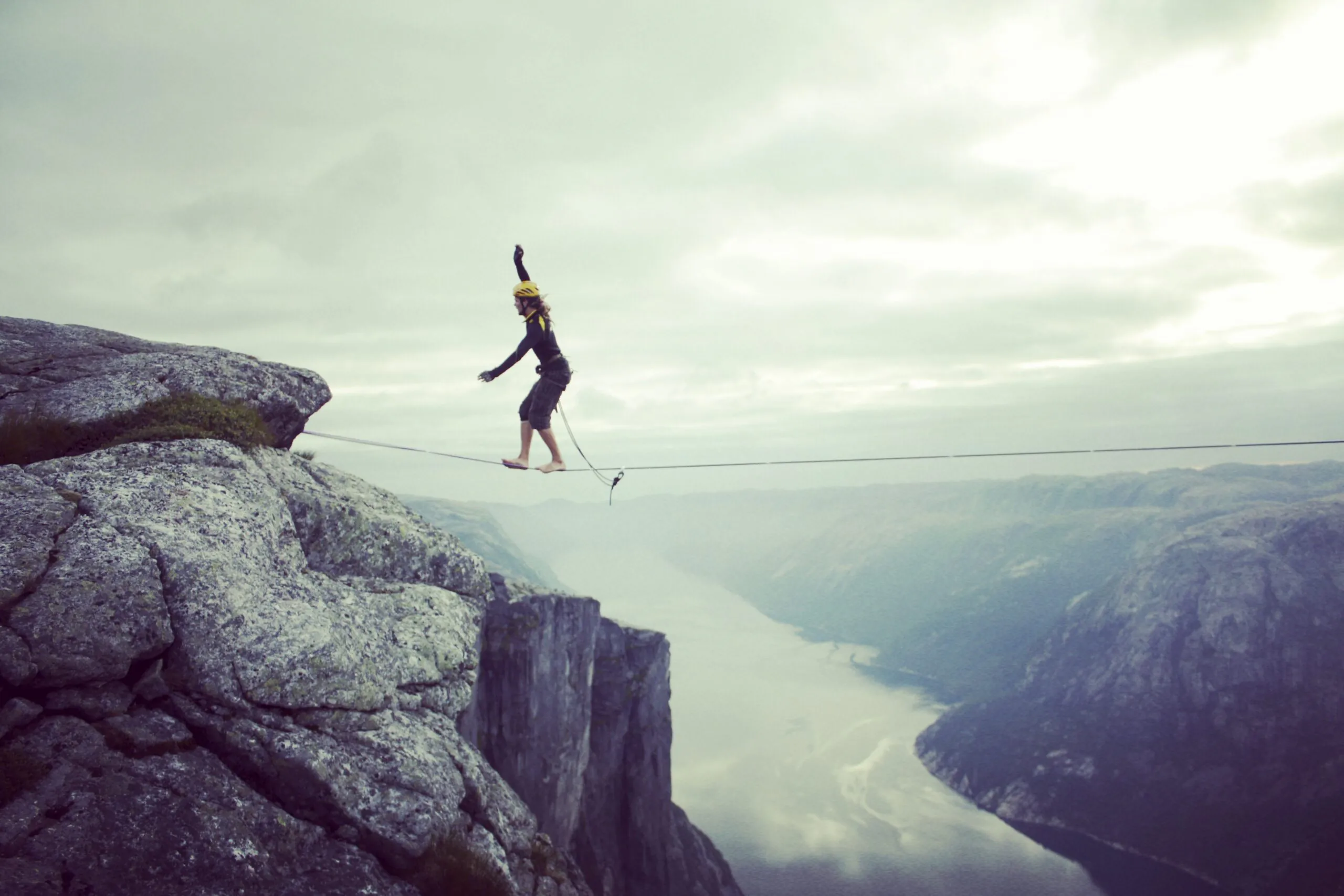 A person walking on a tightrope between cliffs over a misty valley.