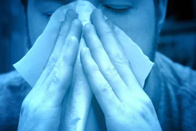 Person blowing nose into tissue, appearing unwell.